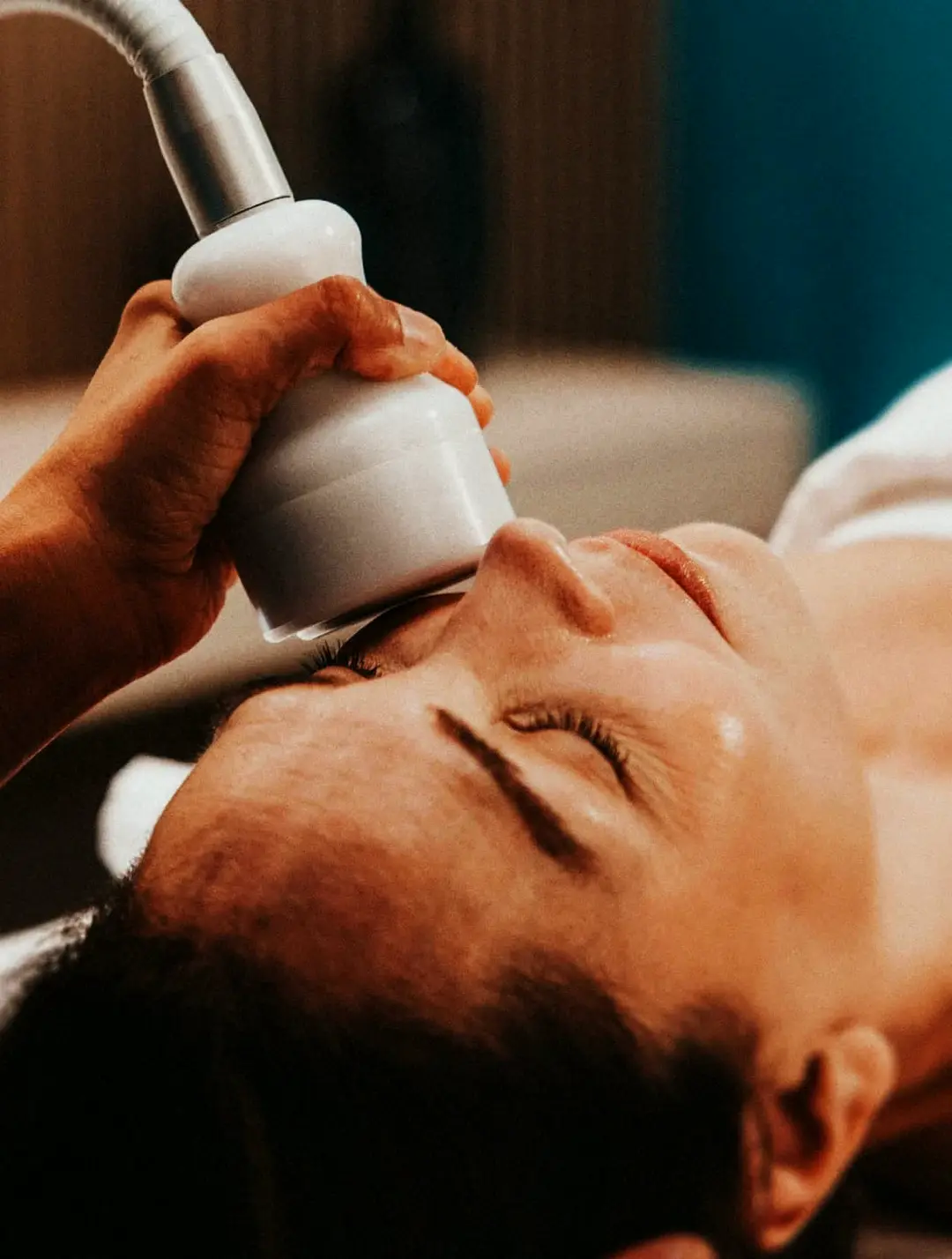 A device-based skin treatment in a teal Hand & Stone treatment room
