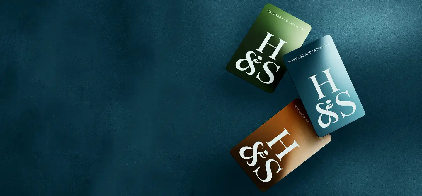 Three Hand & Stone gift cards in green, teal and copper on a dark ground