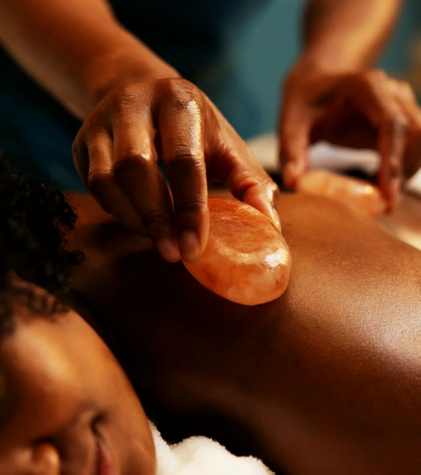 A therapist gliding a warm pink Himalayan salt stone along a guest's back