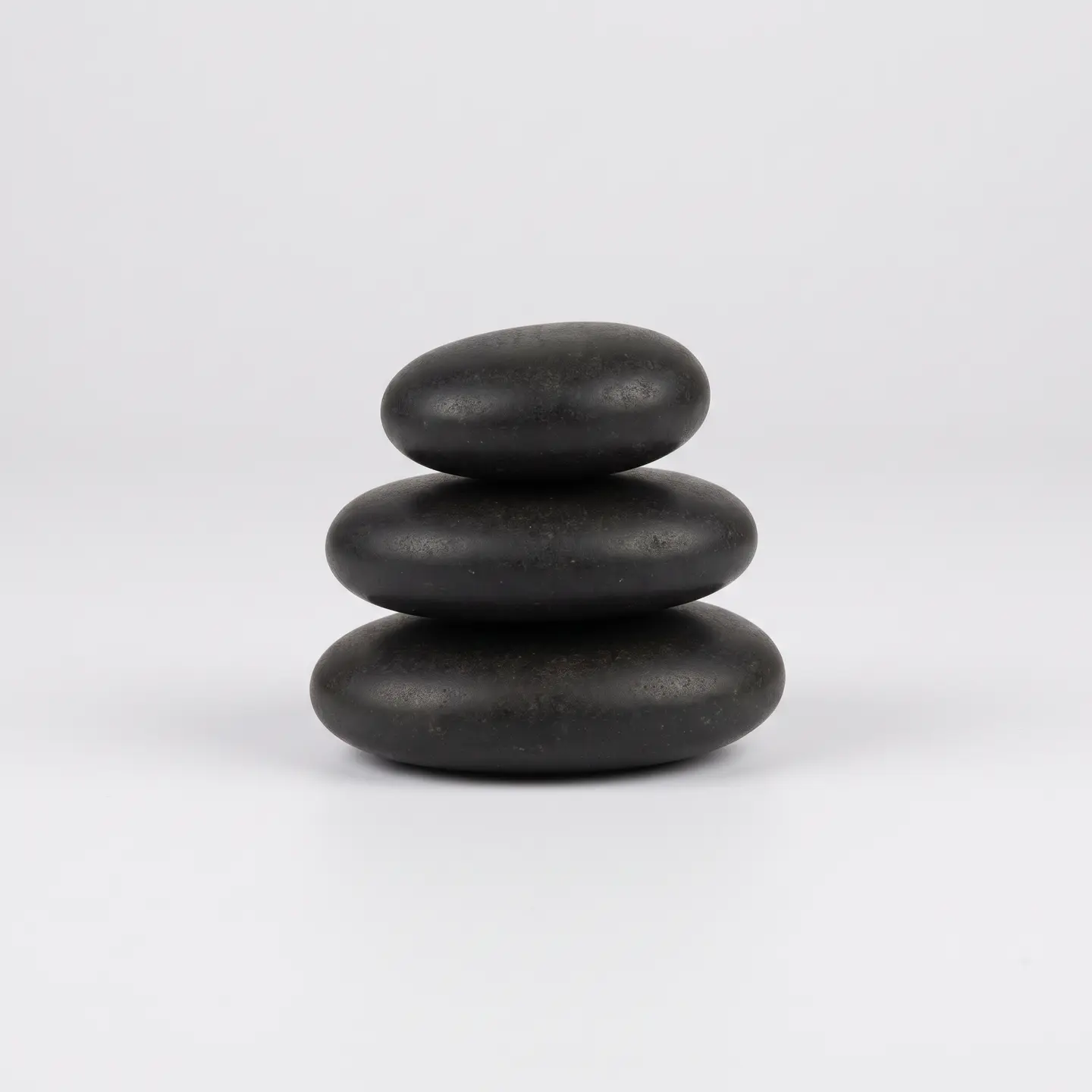 Three smooth, dark massage stones stacked on a pale ground